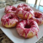 Close-up of air fryer mini donuts with strawberry glaze, arranged on a white plate.