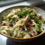 Close-up of a bowl of Apple Cranberry Coleslaw with fresh dill, apples, and cranberries.
