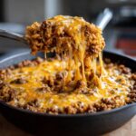 Close-up of a spoonful of One-Pot Cheesy Beef and Rice Skillet with melted cheese, showing a cheese pull.