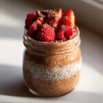 Jar of Chocolate Protein Overnight Oats topped with fresh strawberries and raspberries.