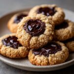 Close-up of several Chocolate Thumbprint Cookies piled on a plate, with rich dark chocolate filling the indentations.
