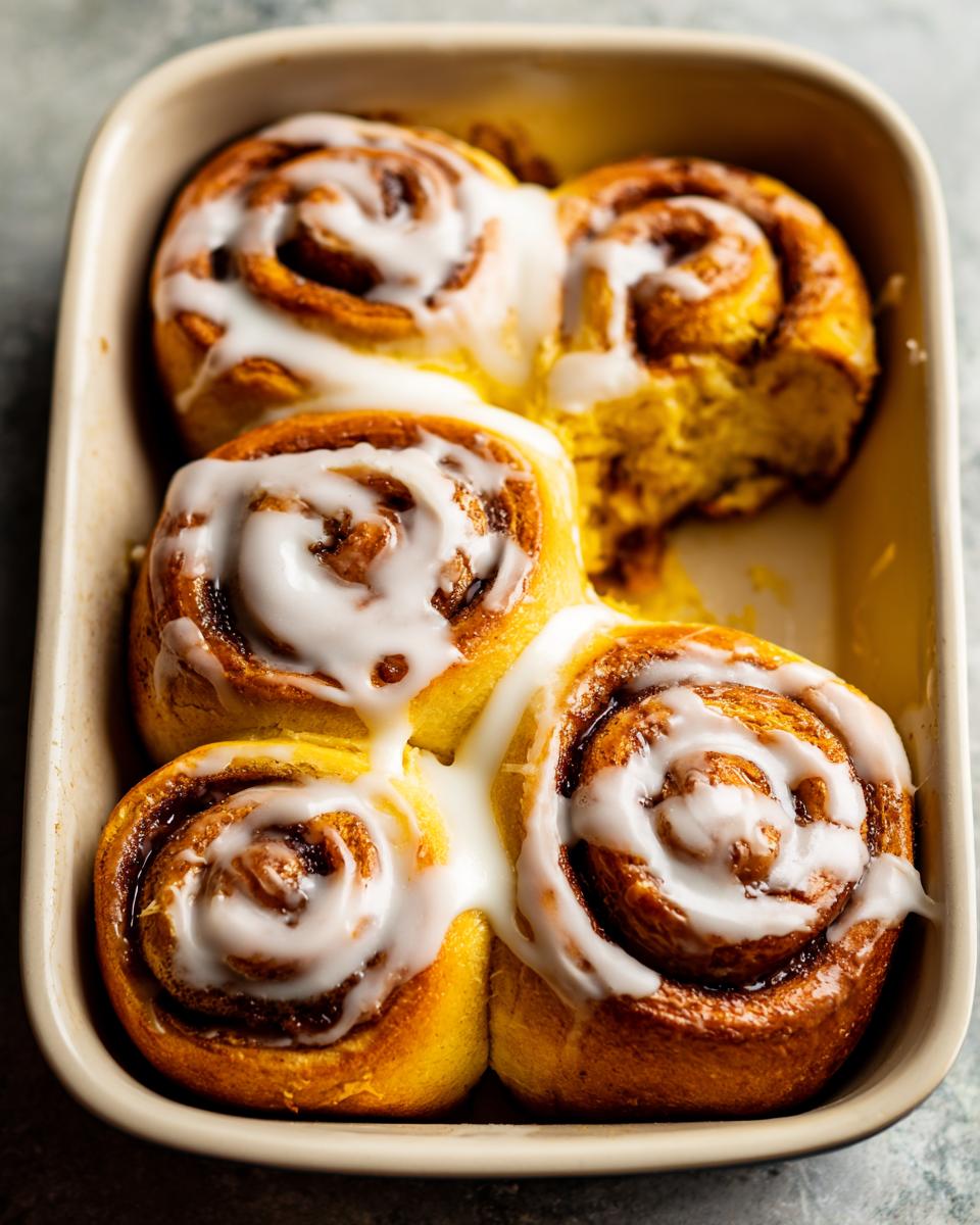 A close-up of freshly baked Christmas Morning Cinnamon Rolls drizzled with white icing in a baking dish.