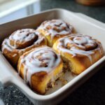 Close-up of four fluffy Christmas Morning Cinnamon Rolls drizzled with white icing in a baking dish.