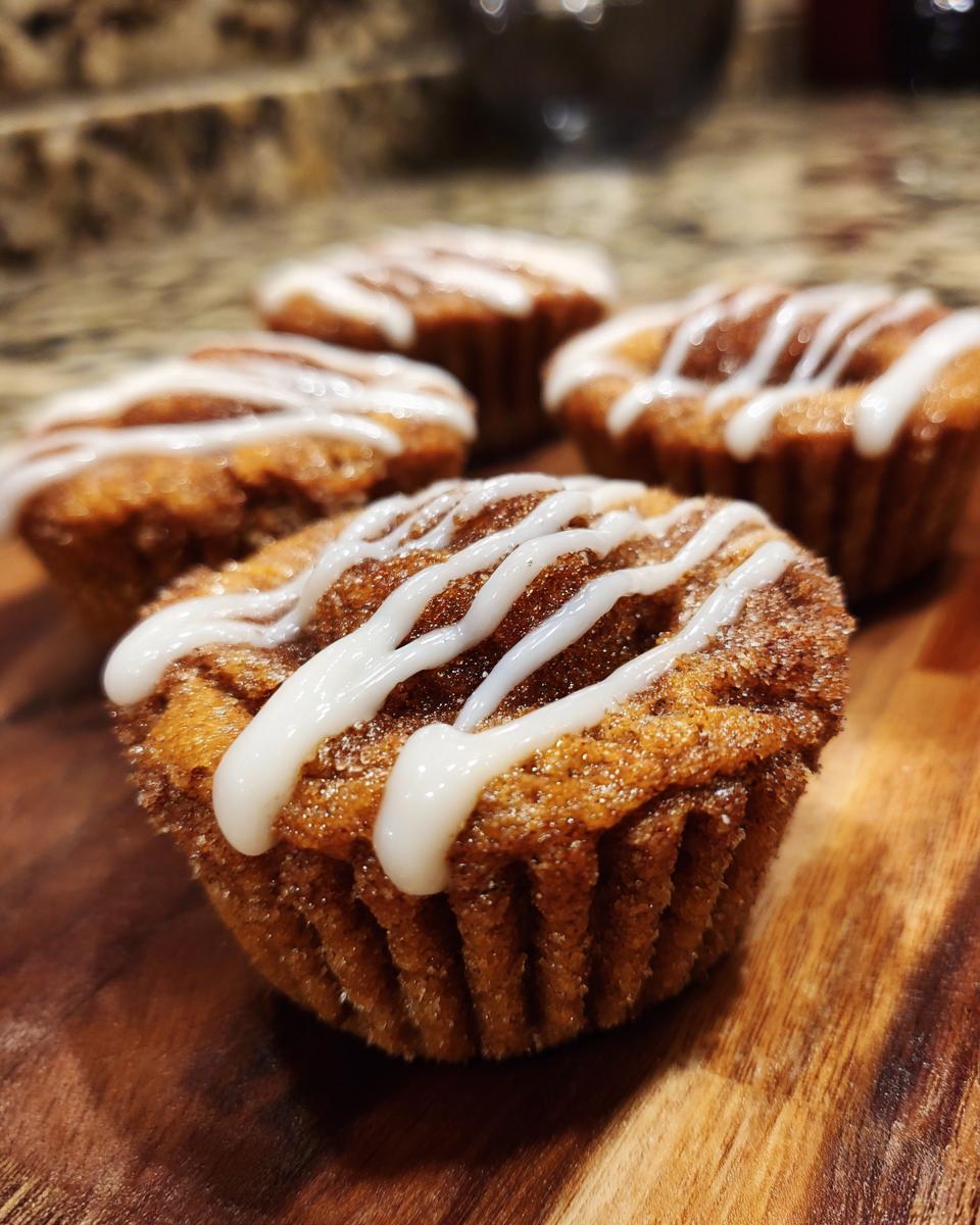 Close-up of several Cinnamon Roll Sugar Cookie Cups drizzled with icing on a wooden board.