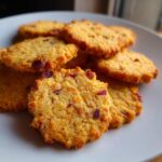 Close-up of delicious Cranberry Orange Shortbread Cookies piled on a white plate, showing their textured surface and dried cranberries.