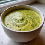 Close-up of a bowl of creamy Broccoli Cheddar Soup, swirled with cream.