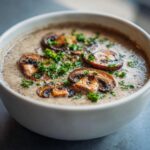 Close-up of a bowl of creamy mushroom soup garnished with fresh parsley.