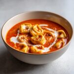 Close-up of a bowl of Creamy Tomato Tortellini Soup with a swirl of cream and herbs.