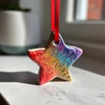 A colorful, glittery star-shaped DIY salt dough ornament for kids, hanging by a red ribbon.