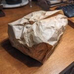 A crumpled brown paper bag sits on a wooden desk, symbolizing eco-friendly gift wrapping.