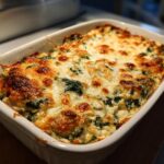 Overhead shot of a baked Four-Cheese Spinach Artichoke Dip Casserole in a white baking dish.