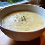 A bowl of creamy Garlic Parmesan Cauliflower Soup, garnished with herbs, on a wooden surface.