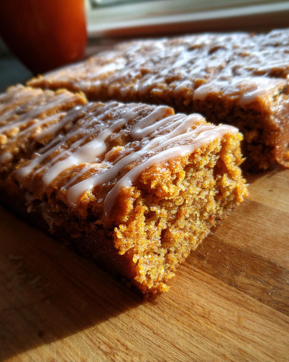Close-up of moist Gingerbread Cookie Bars drizzled with white icing on a wooden board.