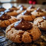 Close-up of a warm Gingerbread Kiss Cookie topped with a swirl of shiny chocolate frosting on a cooling rack.