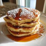 Stack of fluffy Gingerbread Pancakes drizzled with syrup and dusted with powdered sugar.