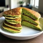 Close-up of a stack of Green Smoothie Oatmeal Pancakes on a white plate, cut to show texture.