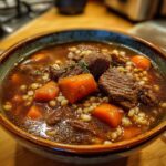 Close-up of a bowl of Hearty Beef & Barley Soup with beef chunks, carrots, and barley.