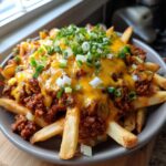 Close-up of a bowl of Hearty Chili Cheese Fries topped with cheese and green onions.