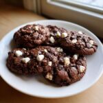 Close-up of several rich chocolate Hot Cocoa Cookies topped with mini marshmallows and chocolate chips.