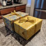 Two beautifully wrapped gifts with gold ribbon, showcasing patterned wrapping paper, demonstrating how to wrap odd-shaped gifts.