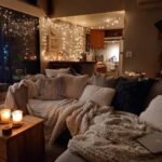 Cozy living room with plush blankets, pillows, candles, and string lights, embodying hygge-inspired winter home decor.
