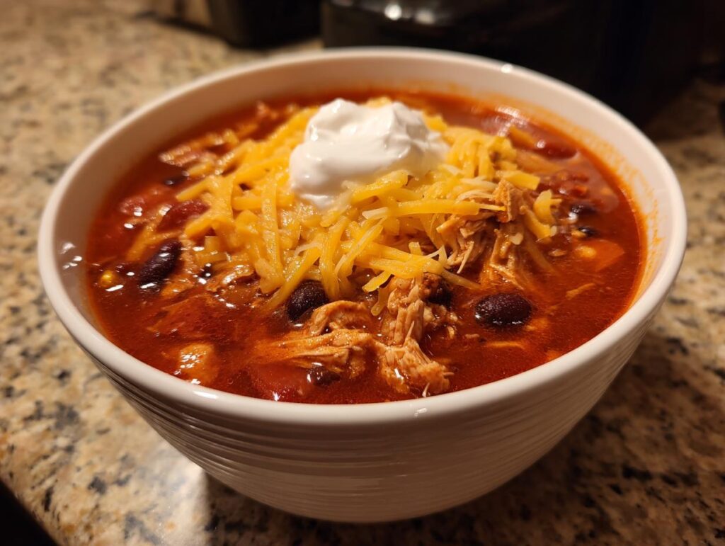 A bowl of delicious Instant Pot Chicken Enchilada Soup, topped with cheese and sour cream.