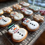 Close-up of several decorated Melted Snowman Sugar Cookies on a wire cooling rack, with snowflake cookies in the background.