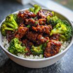 A bowl of One-Pan Honey Soy Chicken and Broccoli served over rice, garnished with green onions.