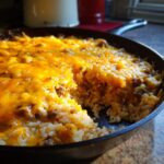 Close-up of a One-Pot Cheesy Beef and Rice Skillet in a cast iron skillet, with a scoop taken out.
