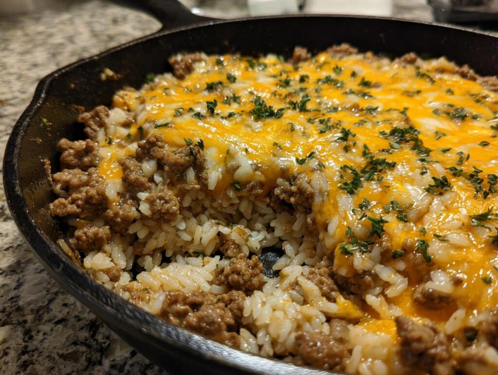 Close-up of a One-Pot Cheesy Beef and Rice Skillet in a cast iron skillet, topped with melted cheese and herbs.