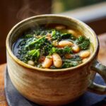 Close-up of a bowl of One-Pot White Bean & Kale Soup, with kale, beans, and broth.