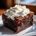 A slice of Peppermint Hot Cocoa Brownie topped with whipped cream, on a white plate.