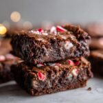 Close-up of stacked Peppermint Hot Cocoa Brownies topped with crushed peppermint candies.