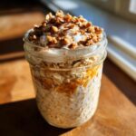 Close-up of Pumpkin Spice Latte Overnight Oats in a jar, topped with whipped cream and granola.