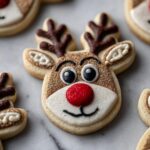 Close-up of a festive Rudolph the Red-Nosed Reindeer sugar cookie with a sparkling red nose and glittery antlers.