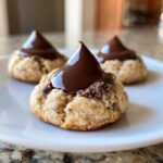 Three Santa's Favorite Peanut Butter Blossoms cookies with chocolate kisses on a white plate.