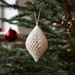 A white, intricate ornament hangs on a branch of a Scandinavian minimal Christmas tree.