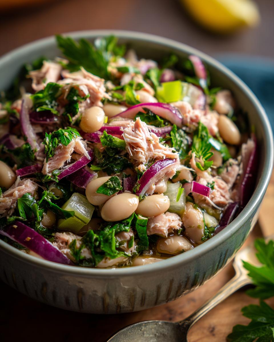Close-up of a bowl of Simple Tuna and White Bean Salad with red onion and parsley.