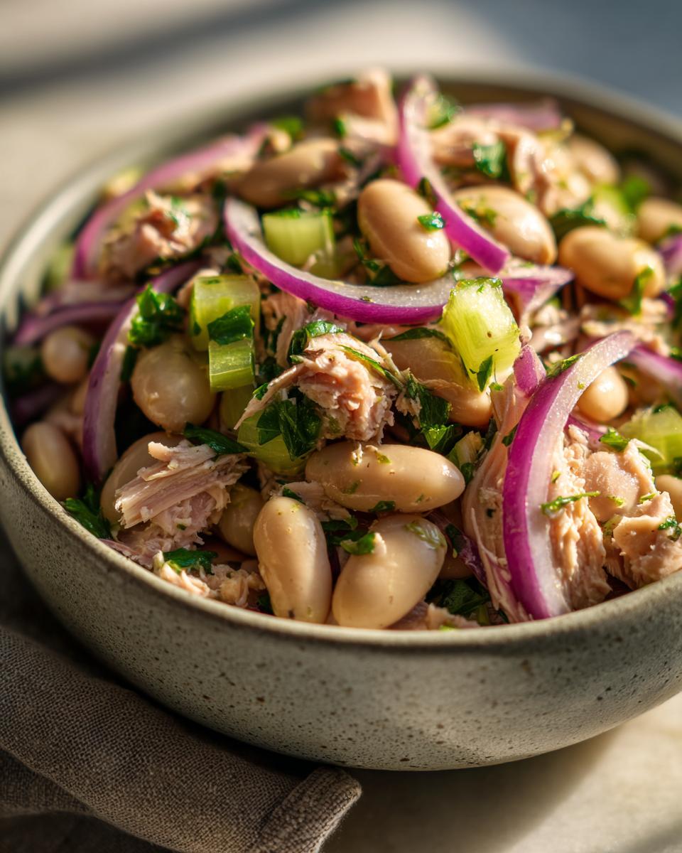Close-up of a bowl of Simple Tuna and White Bean Salad with red onion and parsley.