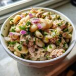 Close-up of a bowl of Simple Tuna and White Bean Salad with red onion and herbs.