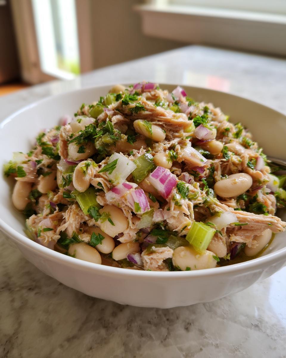 Close-up of a bowl of Simple Tuna and White Bean Salad with tuna, white beans, red onion, and herbs.