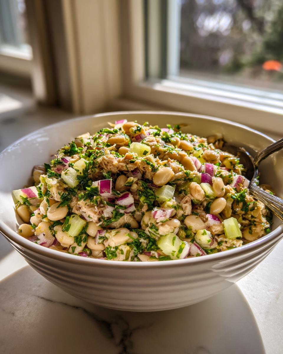 Close-up of a bowl filled with Simple Tuna and White Bean Salad, with tuna, beans, red onion, and herbs.