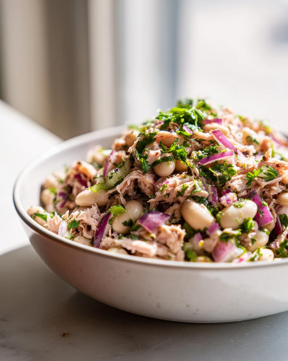 Close-up of a bowl of Simple Tuna and White Bean Salad with red onion and herbs.