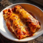Close-up of two Slow Cooker Bean and Cheese Enchiladas in a white bowl, covered in melted cheese.