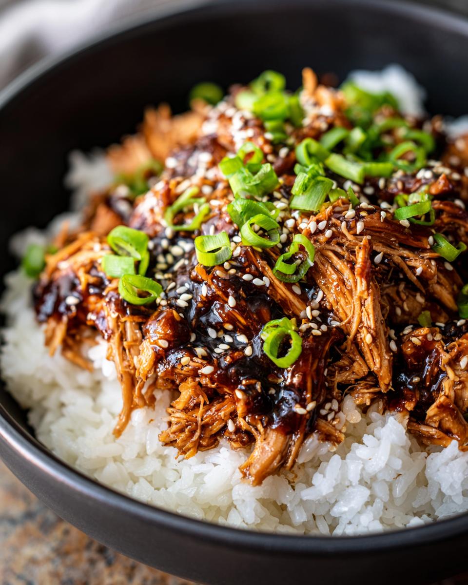 A close-up of shredded Slow Cooker Teriyaki Chicken Recipe served over white rice, garnished with green onions and sesame seeds.