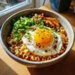 Close-up of a bowl of spicy ramen noodle soup with a fried egg and green onions.