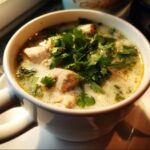 A bowl of Thai-Inspired Coconut Chicken Soup with chicken and cilantro.