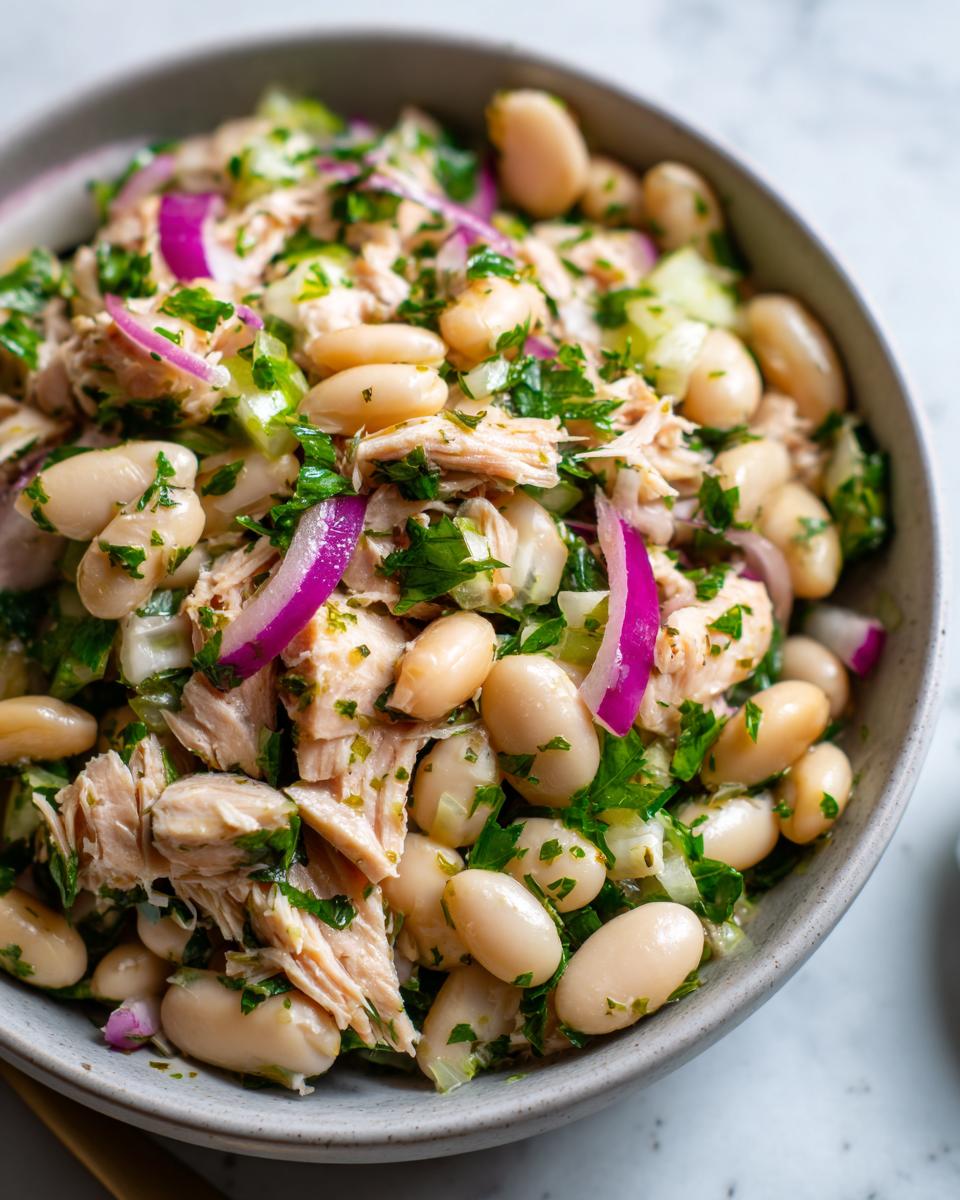 Close-up of a bowl of Simple Tuna and White Bean Salad with red onion and parsley.