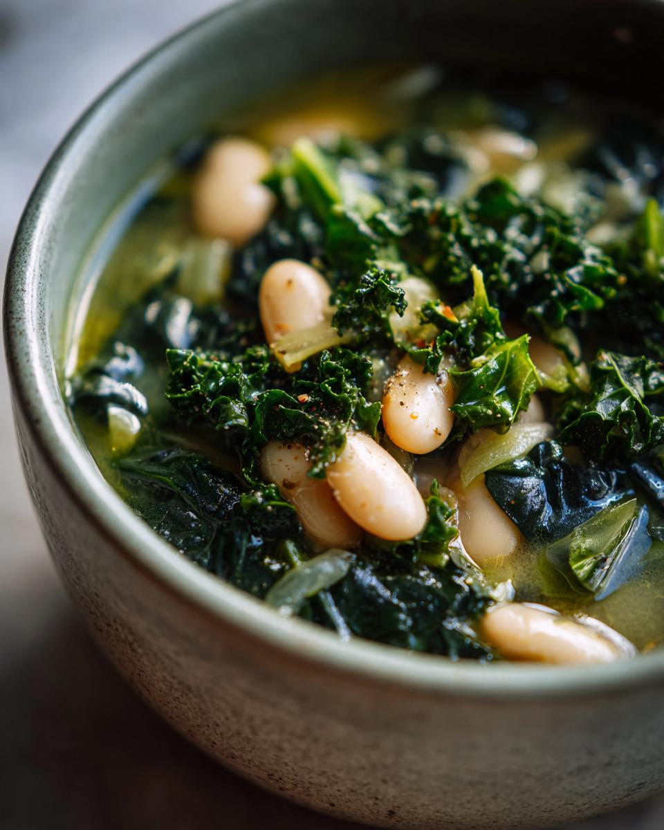Close-up of a bowl of Tuscan White Bean & Kale Soup, showing beans, kale, and broth.