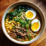 A flavorful upgraded ramen bowl with garlic butter, soft boiled eggs, corn, and greens.